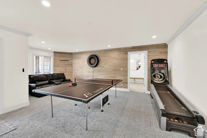 Rec room with wood walls, ornamental molding, recessed lighting, light colored carpet, and an accent wall