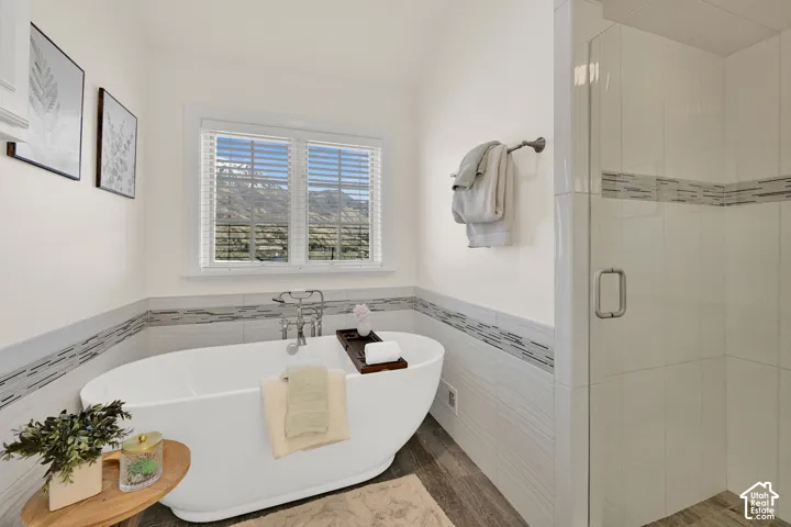 Full bathroom with a soaking tub, tile walls, wainscoting, a shower stall, and wood finished floors