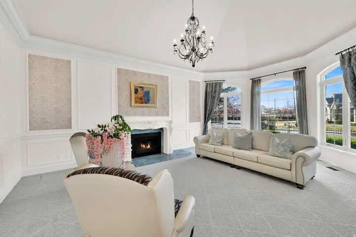 Living room with a decorative wall, a fireplace, hanging lights, light carpet, and crown molding