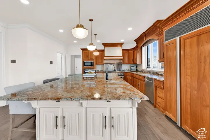 Kitchen featuring built in appliances, a breakfast bar, light stone countertops, a large island, and hanging light fixtures