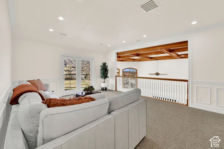 Carpeted living area featuring a decorative wall, coffered ceiling, a wainscoted wall, ceiling fan, and recessed lighting