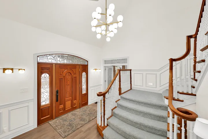 Entryway with a decorative wall, a wainscoted wall, wood finished floors, a chandelier, and vaulted ceiling
