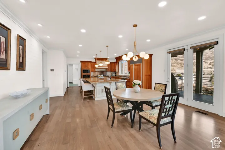 Dining room with light wood finished floors, crown molding, and suspended lighting