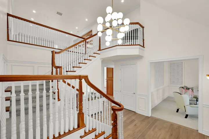 Stairway with a high ceiling, a decorative wall, wood finished floors, a chandelier, and wainscoting