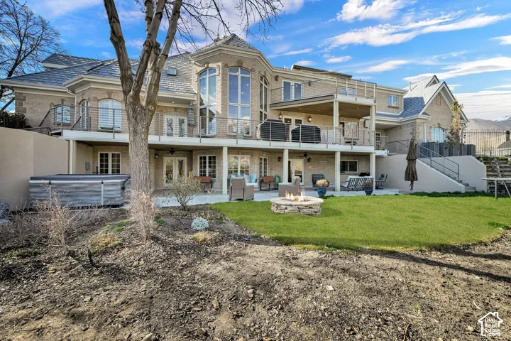 Back of house featuring a hot tub, a patio area, a balcony, brick siding, and an outdoor living space with a fire pit