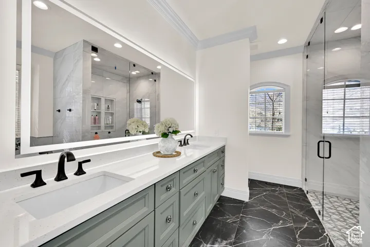 Bathroom with double vanity, a marble finish shower, dark marble finish flooring, ornamental molding, and recessed lighting