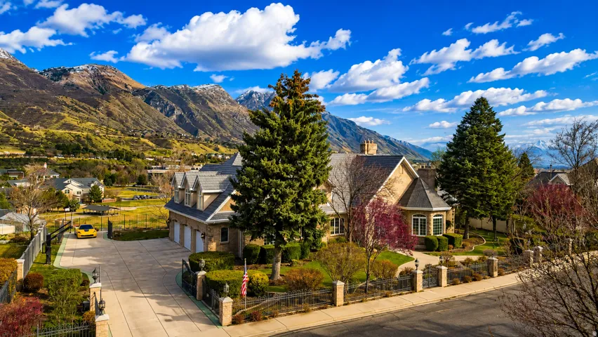 Stone facade residence featuring a multi-car garage, established landscaping, and a paved driveway with gated entry