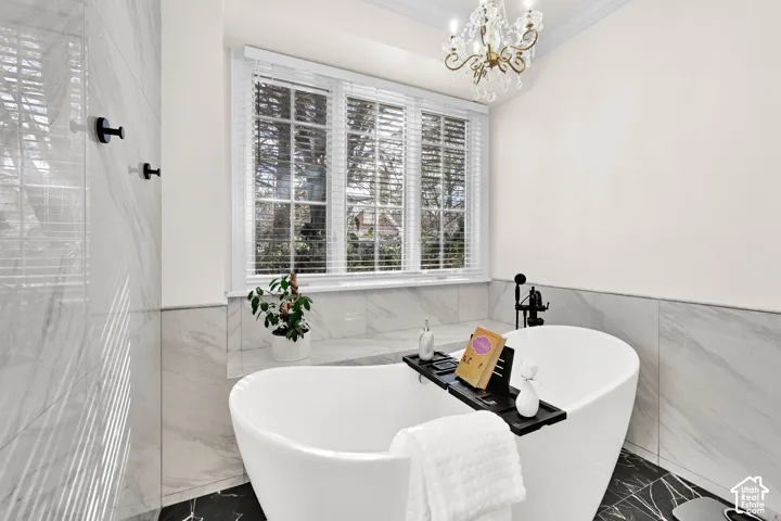 Bathroom with ornamental molding, a freestanding bath, tile walls, a wainscoted wall, and hanging lights