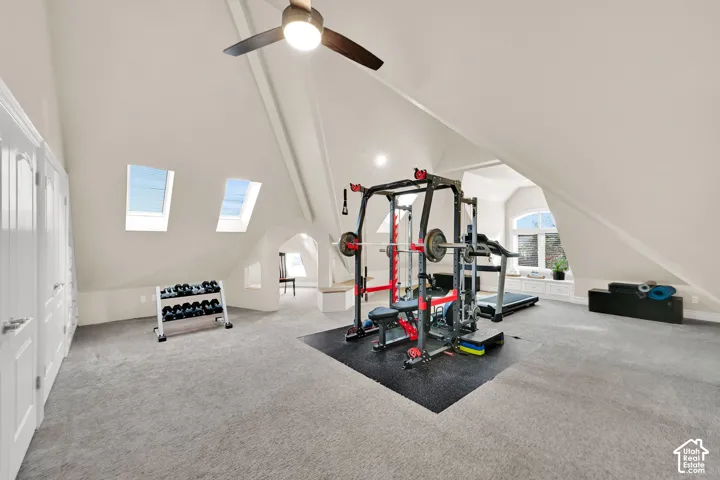 Exercise area featuring light colored carpet, vaulted ceiling, arched walkways, and a ceiling fan