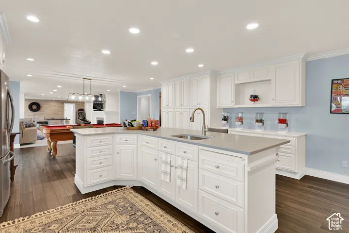 Kitchen with white cabinets, a large island, a fireplace, crown molding, and pendant lighting