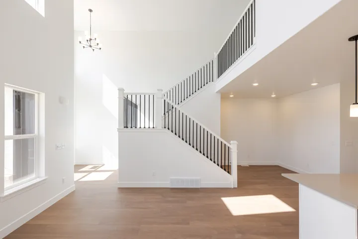 Two-story entryway featuring a white staircase with black iron balusters, wood-finish flooring, high ceilings, and an overhead chandelier