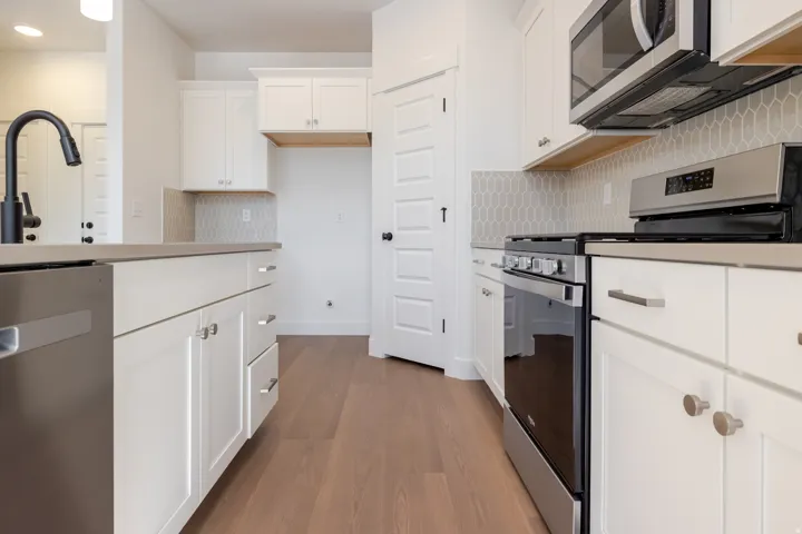 Kitchen featuring white cabinetry, stainless steel appliances, light-toned countertops, a geometric pattern backsplash, and wood-finish flooring