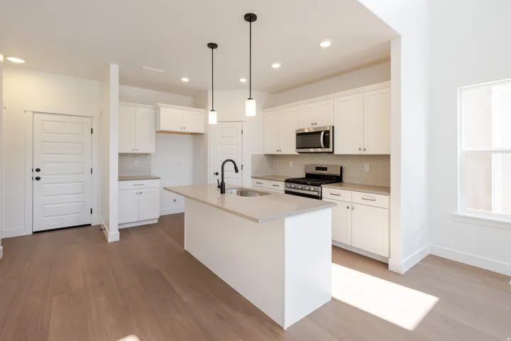 Kitchen featuring white cabinetry, a central island with a sink, stainless steel appliances, a gas range, and wood-finish flooring