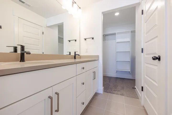 Bathroom featuring a double vanity with matte black faucets, integrated sinks, light-toned countertops, and white cabinetry