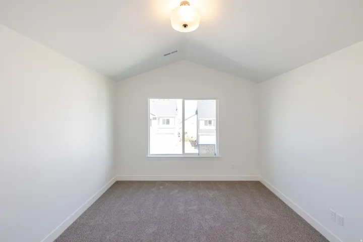 Room with a vaulted ceiling, neutral carpet flooring, and a double window