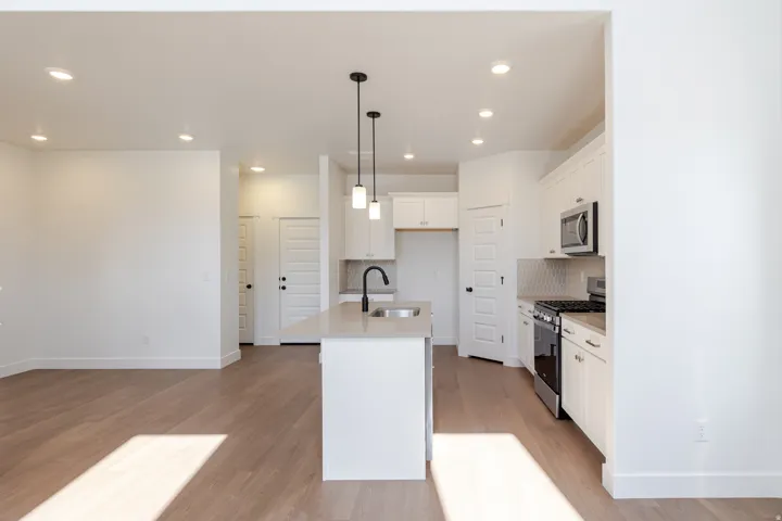 Modern kitchen featuring a central island with an undermount sink, pendant lighting, stainless steel appliances, and wood-finish flooring