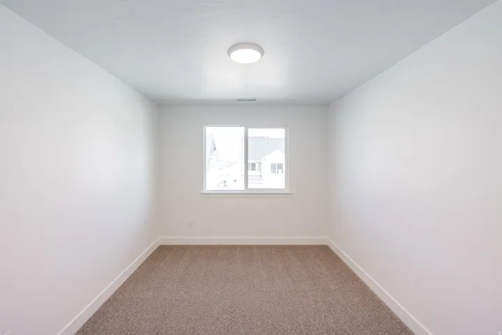 Bright room with a neutral color palette, featuring a double-pane window, flush-mount ceiling light fixture, white baseboards, and textured carpeting