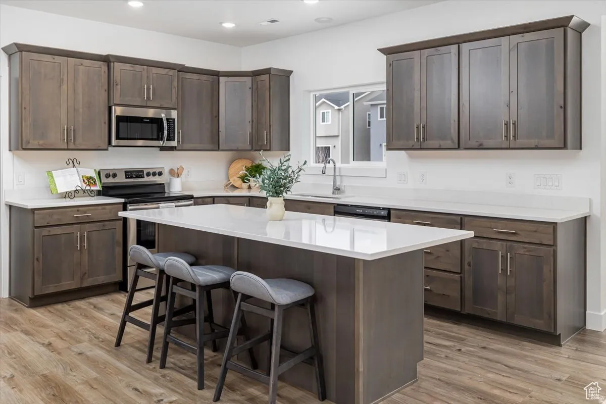 Kitchen with dark wood finish cabinets, stainless steel appliances, a kitchen bar, light wood-style floors, and recessed lighting