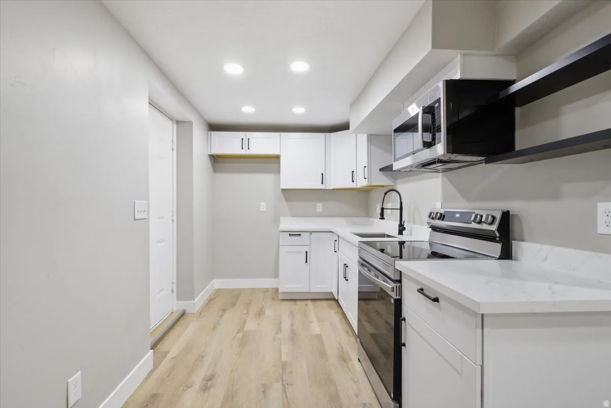 Kitchen with stainless steel appliances, light wood finished floors, white cabinets, recessed lighting, and light stone counters