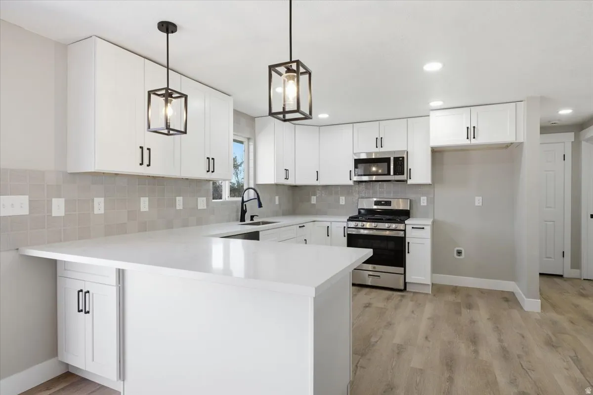 Kitchen featuring stainless steel appliances, a peninsula, white cabinetry, hanging light fixtures, and light wood-style floors