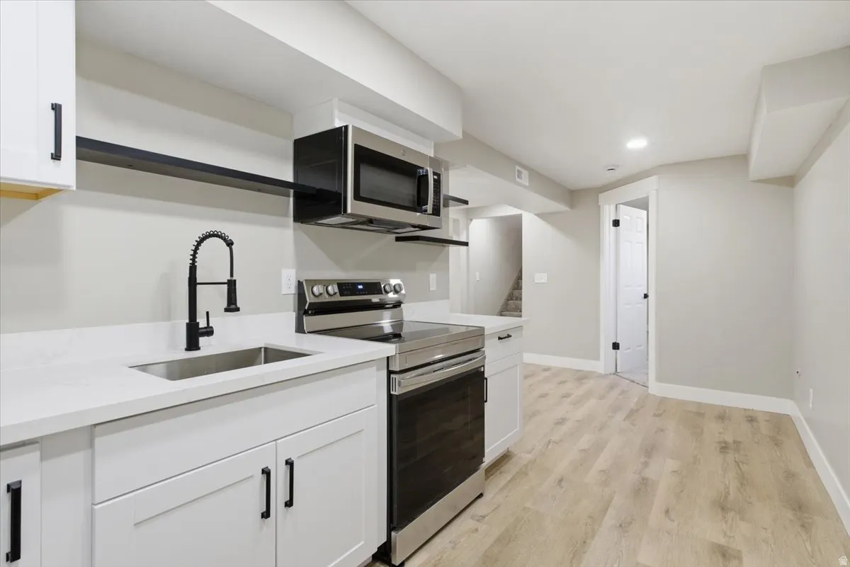 Kitchen with stainless steel appliances, open shelves, white cabinets, light wood finished floors, and light stone countertops