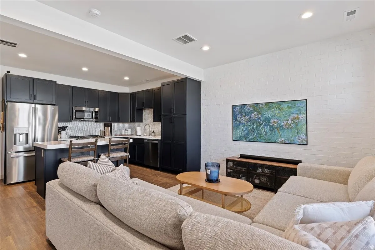 Living area with light wood finished floors, recessed lighting, and brick wall