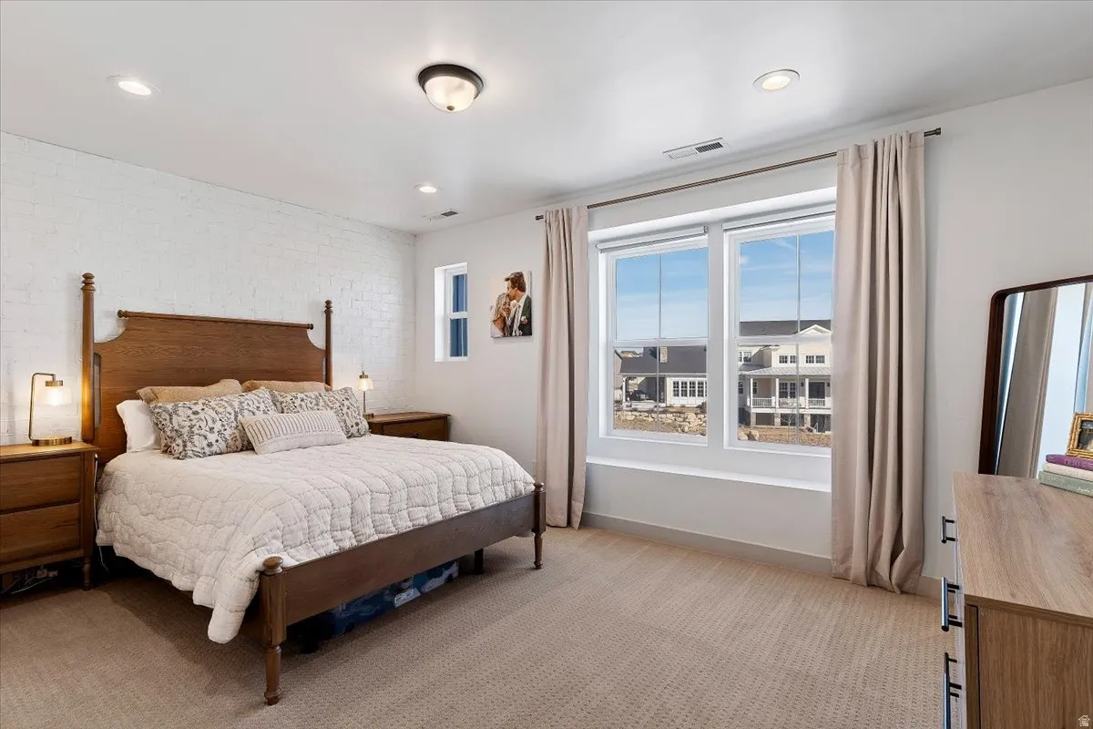 Bedroom featuring light carpet, brick wall, and recessed lighting