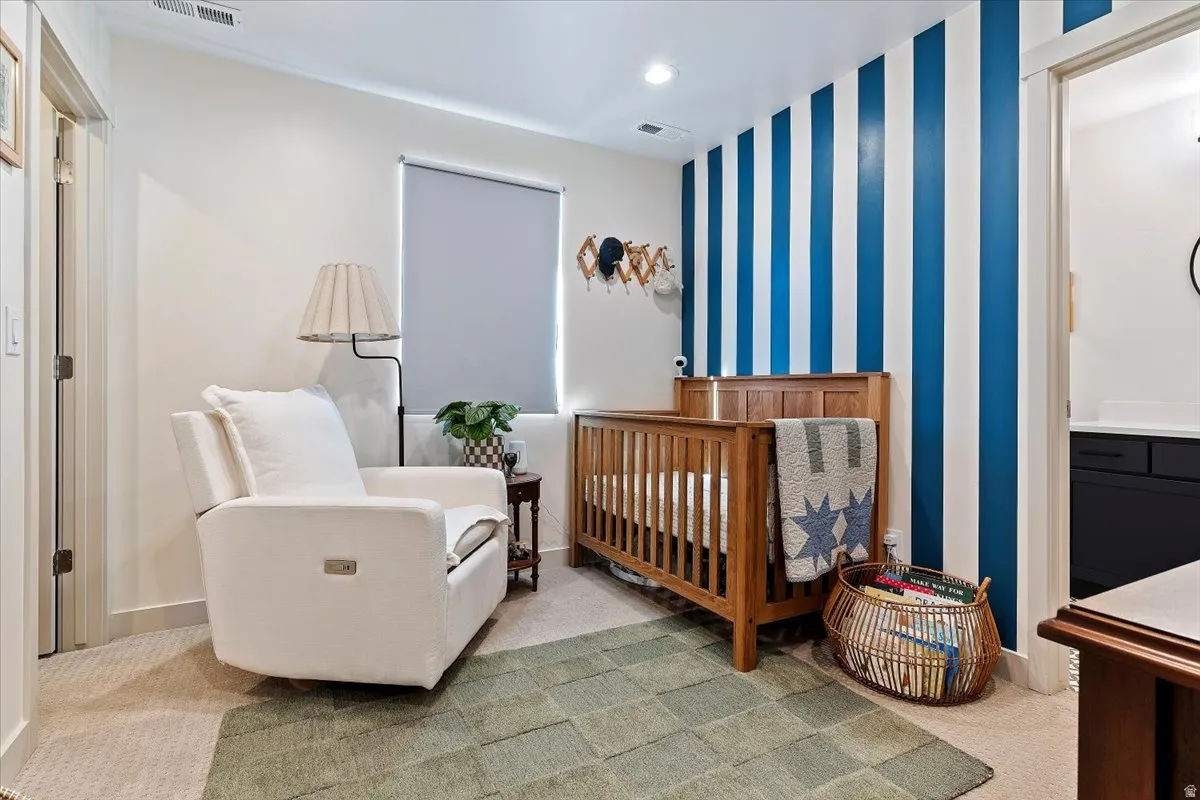 Bedroom with wallpapered walls, a nursery area, an accent wall, light colored carpet, and recessed lighting