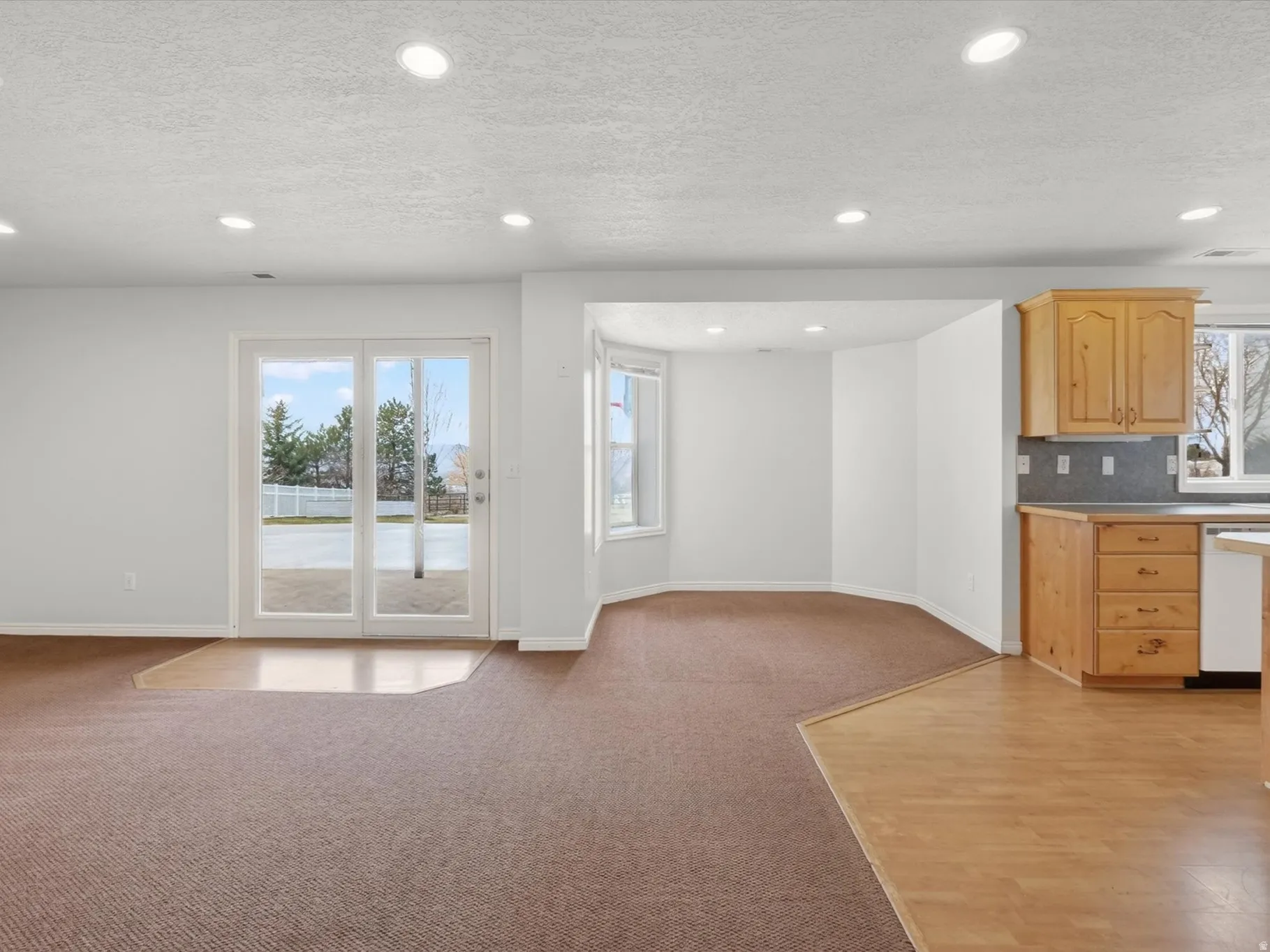 Kitchen featuring a textured ceiling, light wood finish cabinets, light carpet, dishwasher, and open floor plan