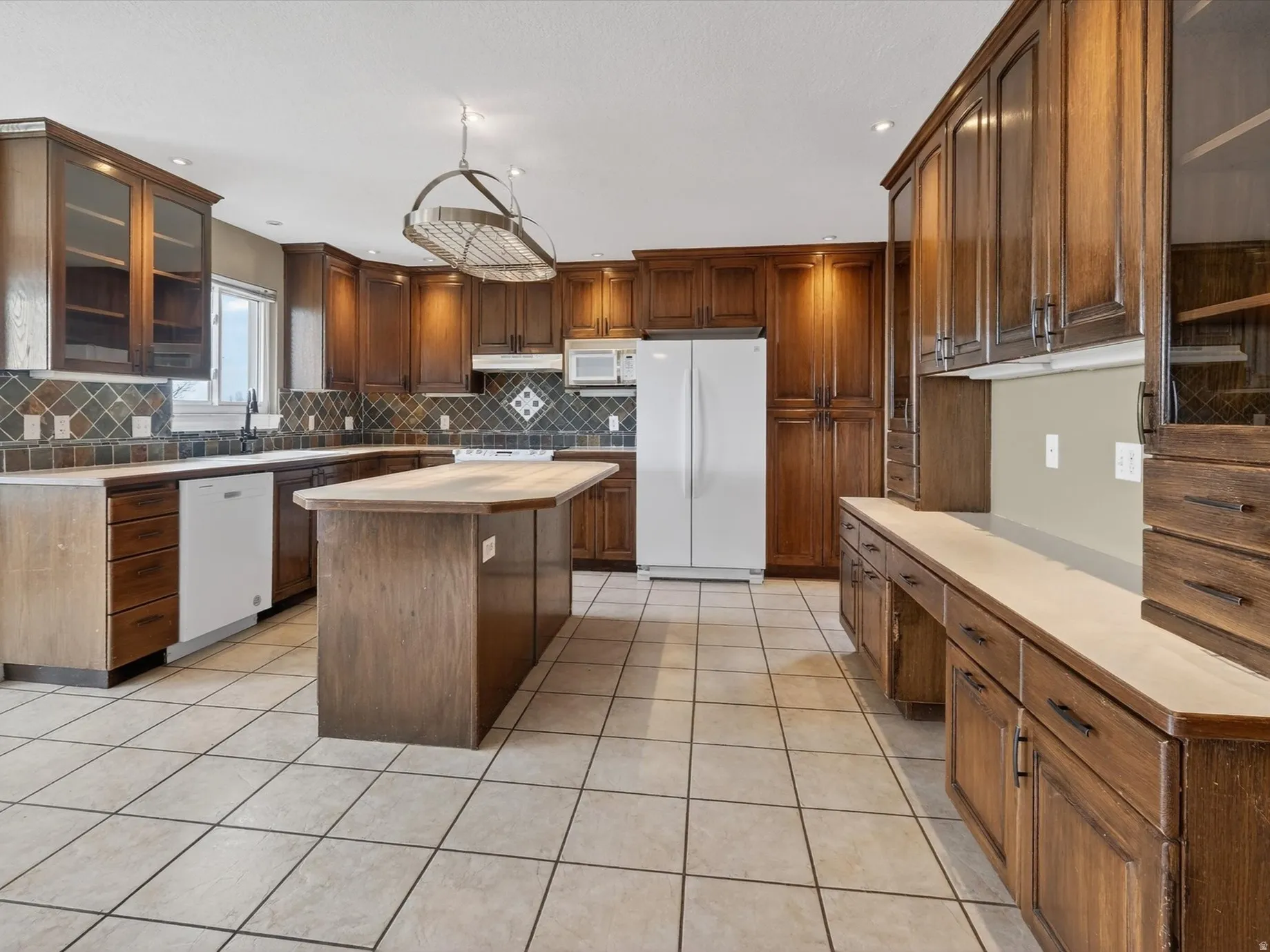 Kitchen featuring glass fronted cabinets, white appliances, a center island, light tile patterned flooring, and wood finish cabinetry