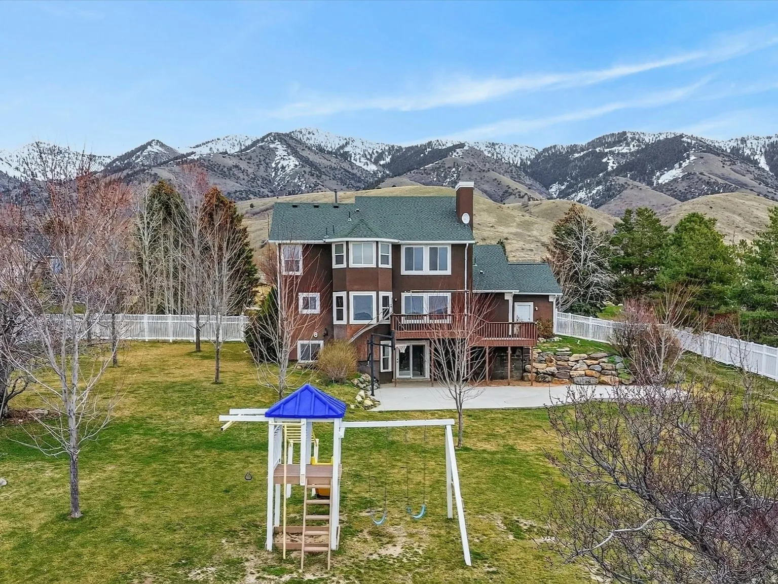 Rear view of house featuring a deck with mountain view, a chimney, a patio area, and a fenced backyard