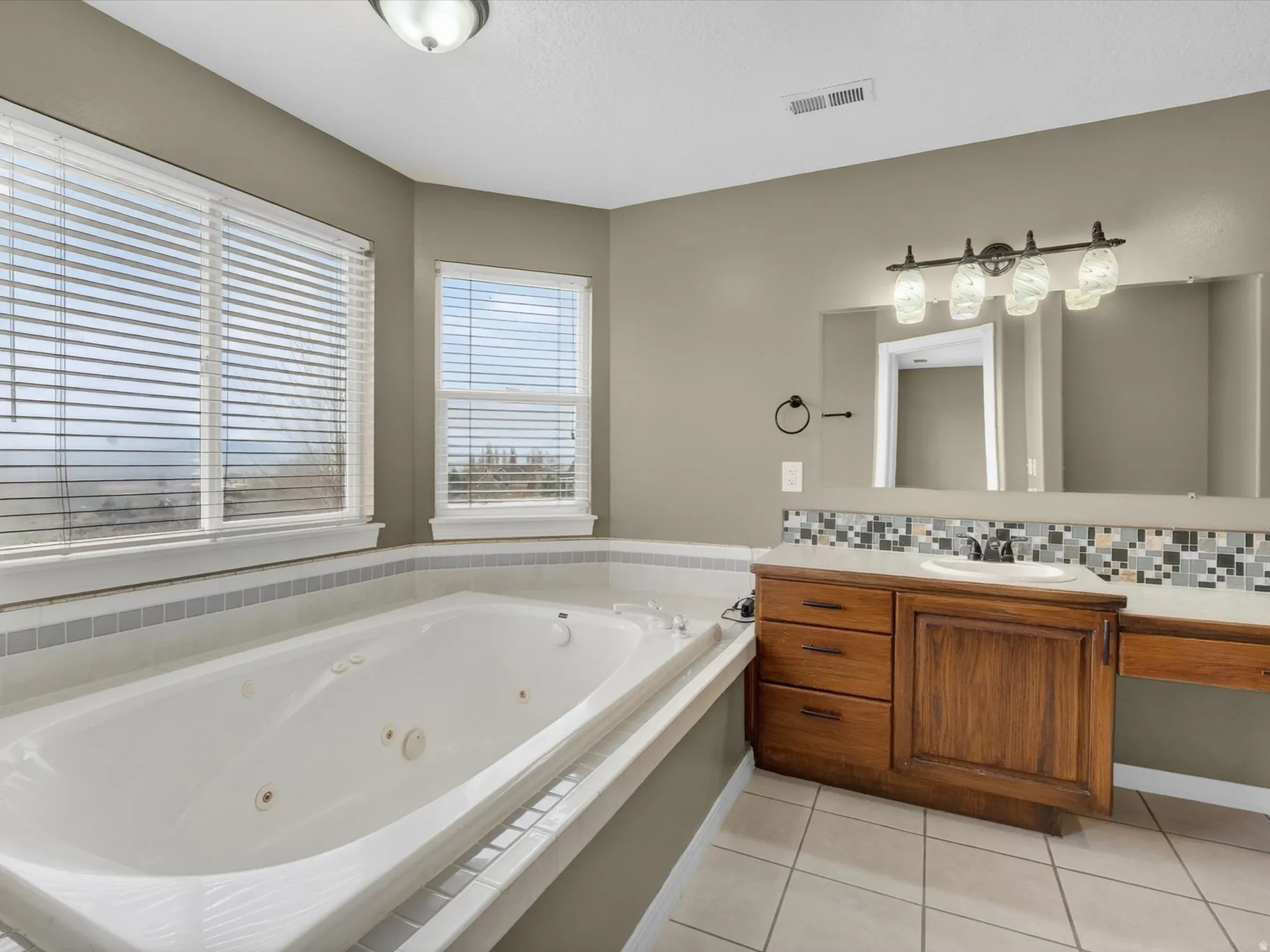 Bathroom featuring vanity, light tile patterned floors, a whirlpool tub, and decorative backsplash