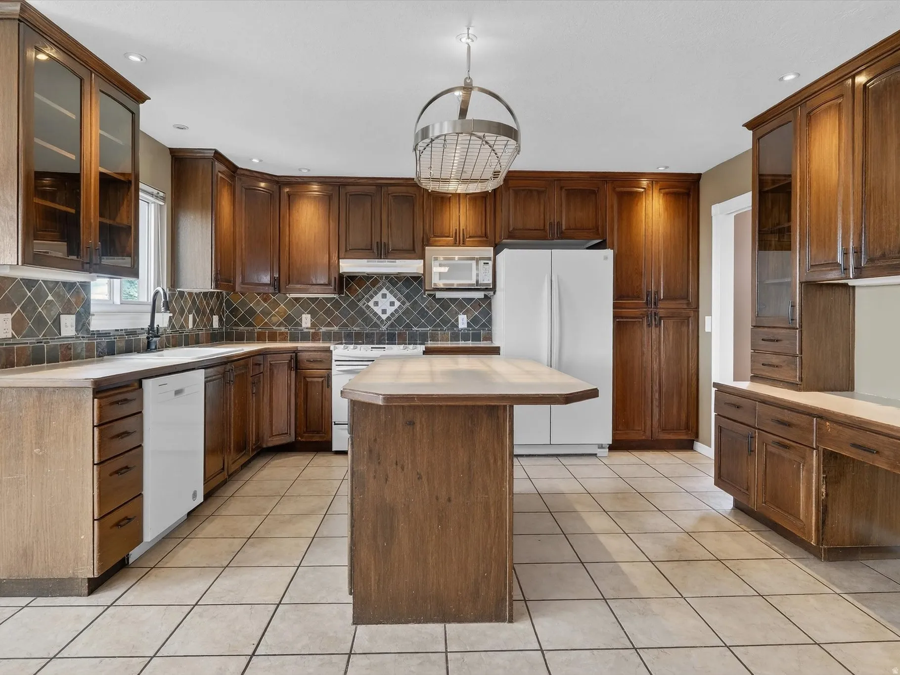 Kitchen with glass fronted cabinets, light countertops, white appliances, light tile patterned floors, and a center island