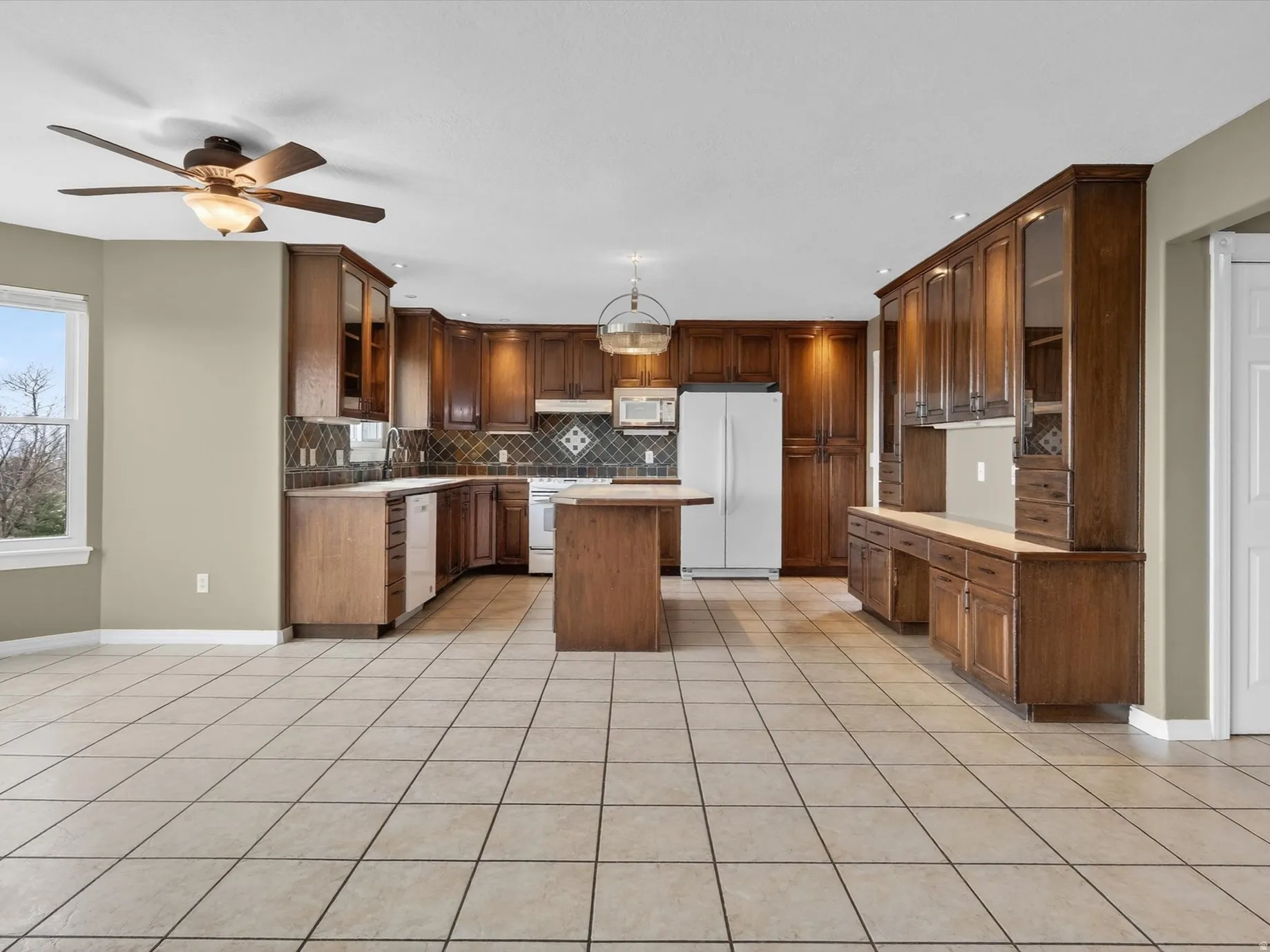Kitchen featuring glass insert cabinets, a kitchen island, light countertops, and white appliances