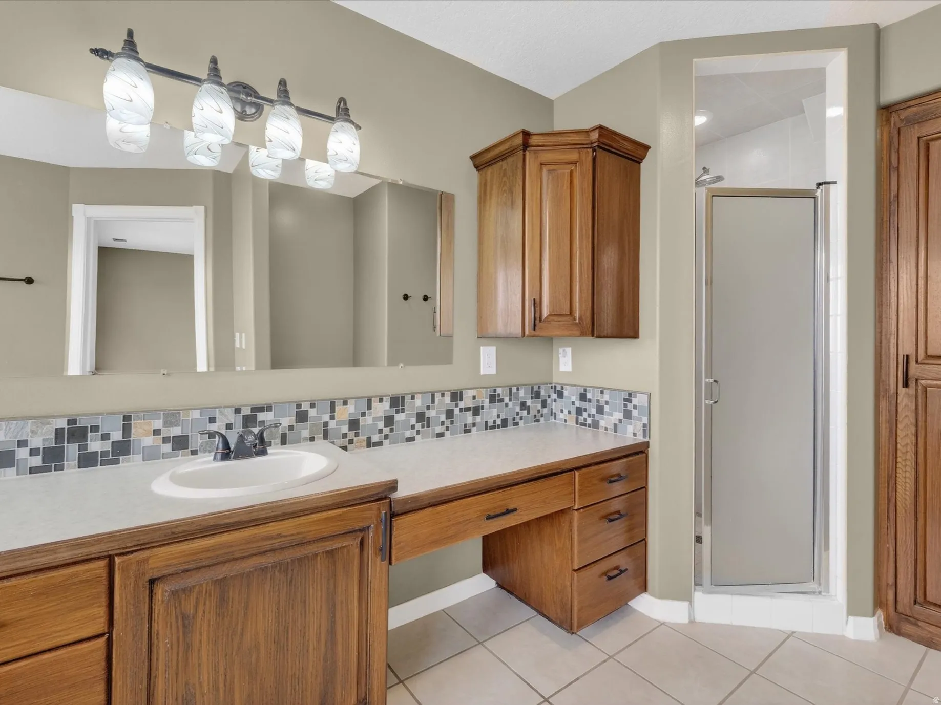Bathroom with backsplash, a stall shower, vanity, and light tile patterned floors
