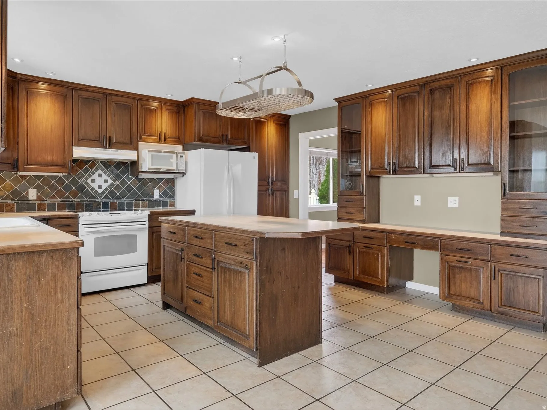 Kitchen featuring white appliances, light tile patterned flooring, a center island, light countertops, and tasteful backsplash
