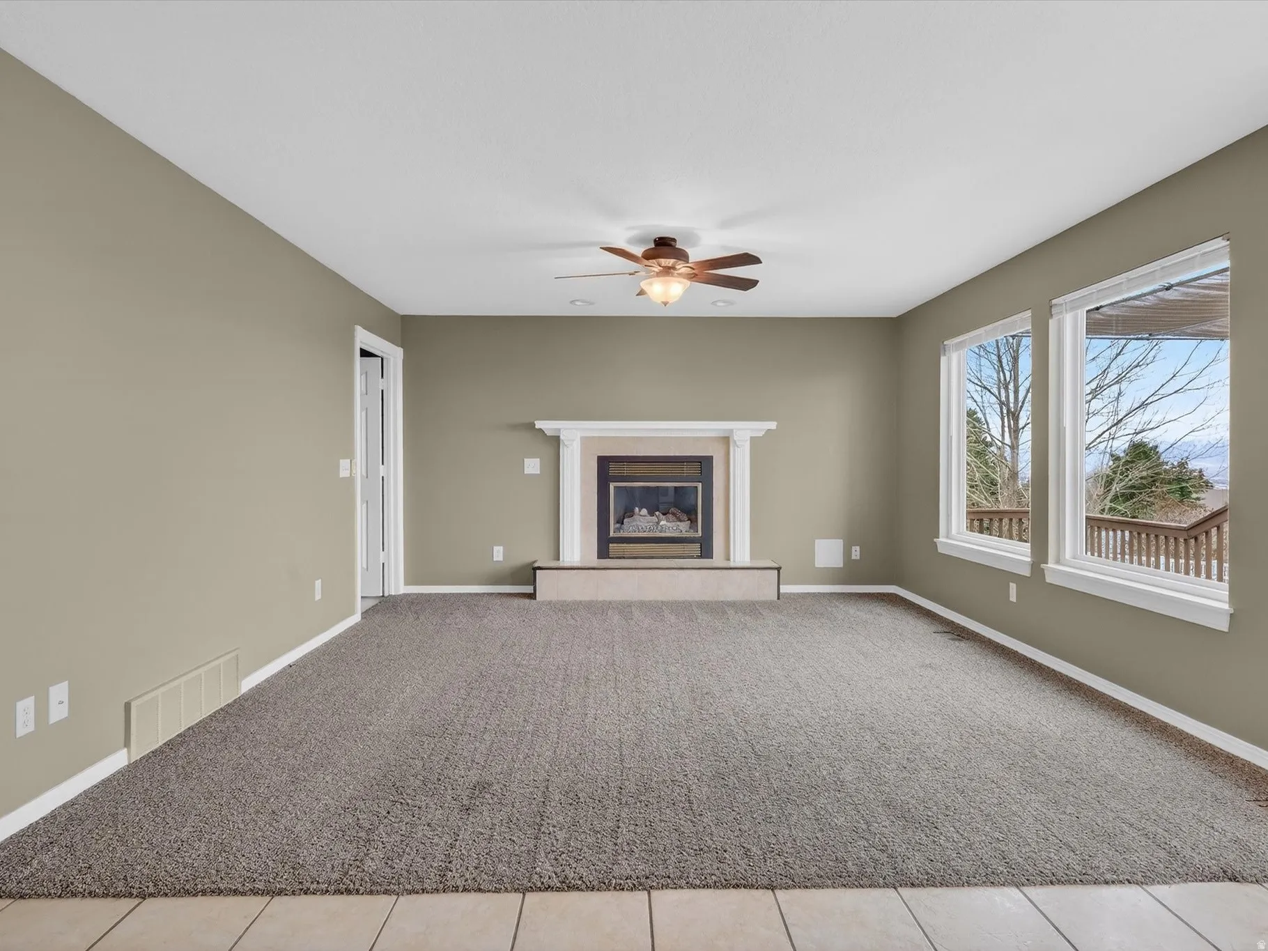 Unfurnished living room featuring light carpet, a glass covered fireplace, and ceiling fan