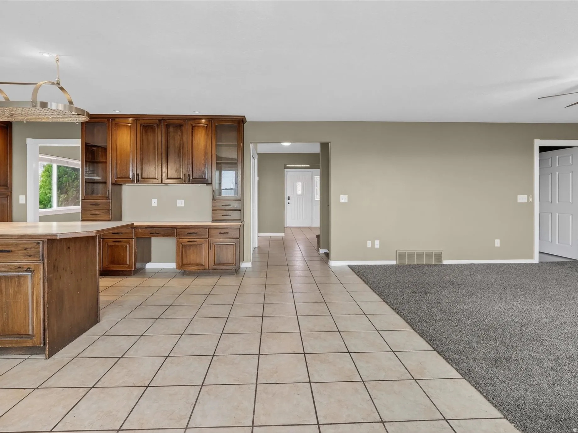 Kitchen with light tile patterned flooring, light countertops, light carpet, wood finish cabinetry, and ceiling fan