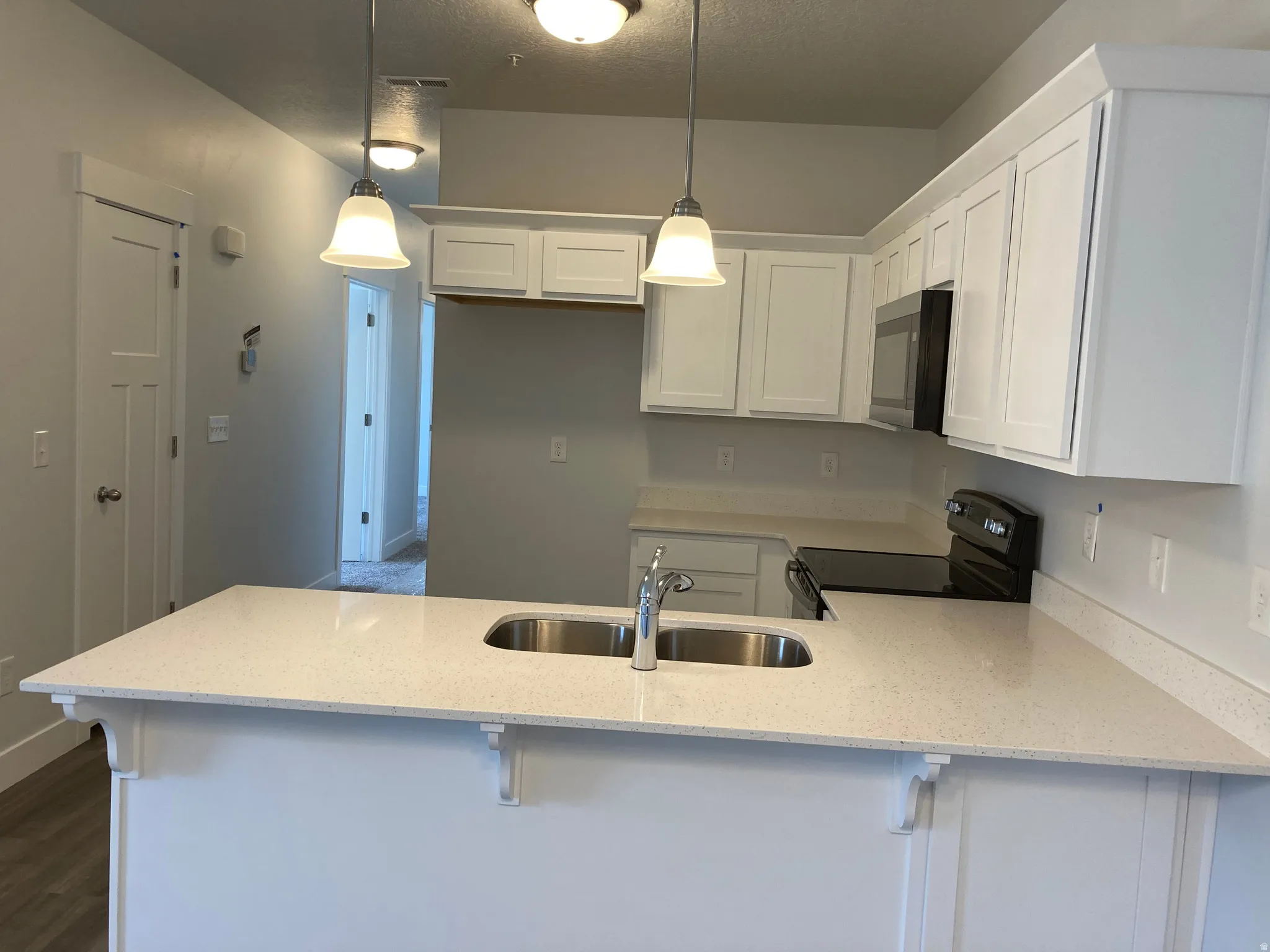 Kitchen featuring a peninsula, a breakfast bar, black range with electric cooktop, white cabinets, and a textured ceiling