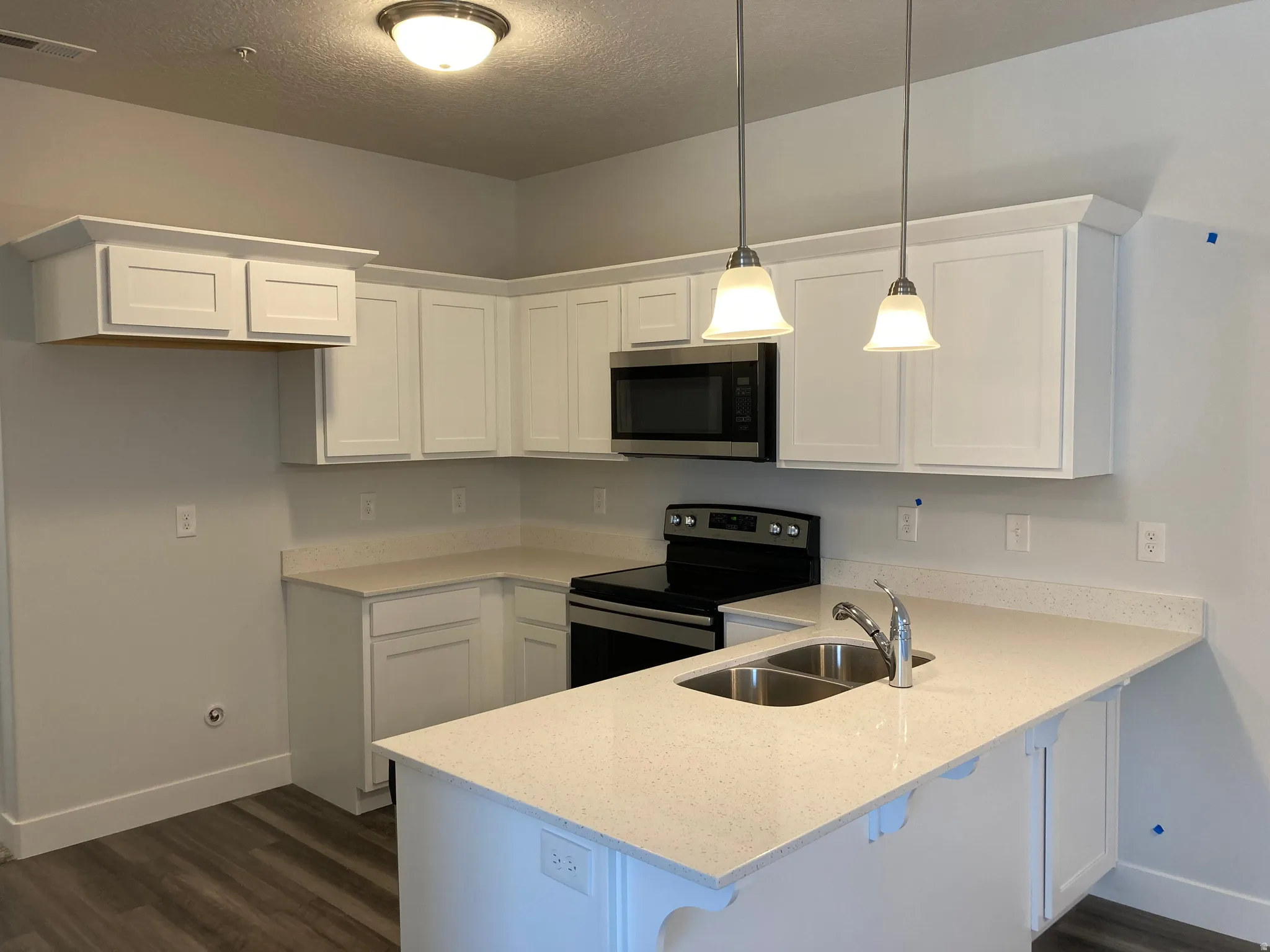 Kitchen with stainless steel appliances, a peninsula, white cabinets, and a textured ceiling
