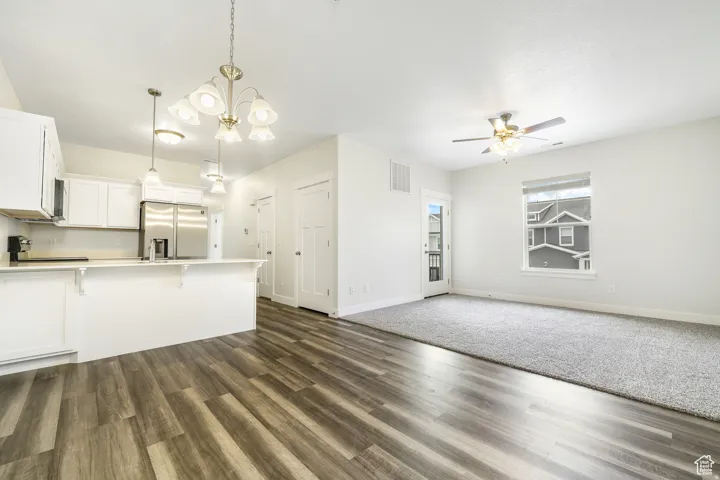 Kitchen with white cabinetry, hanging lights, light countertops, stainless steel fridge with ice dispenser, and open floor plan