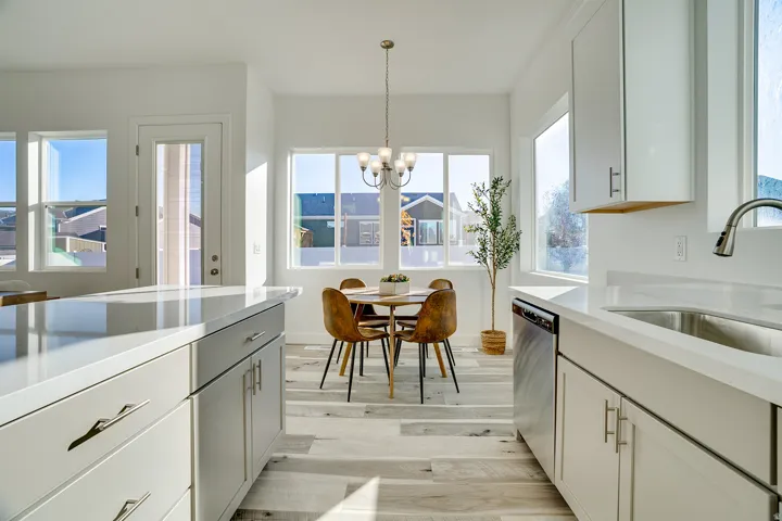 Kitchen with white cabinetry, light stone counters, light wood-style floors, stainless steel dishwasher, and suspended lighting