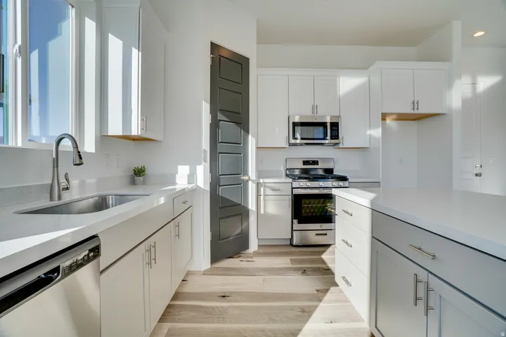 Kitchen featuring stainless steel appliances, light stone counters, white cabinetry, and light wood-style flooring