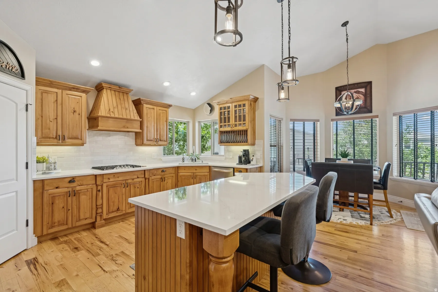 Kitchen with light wood-style floors, glass fronted cabinets, wood finish cabinetry, and vaulted ceiling