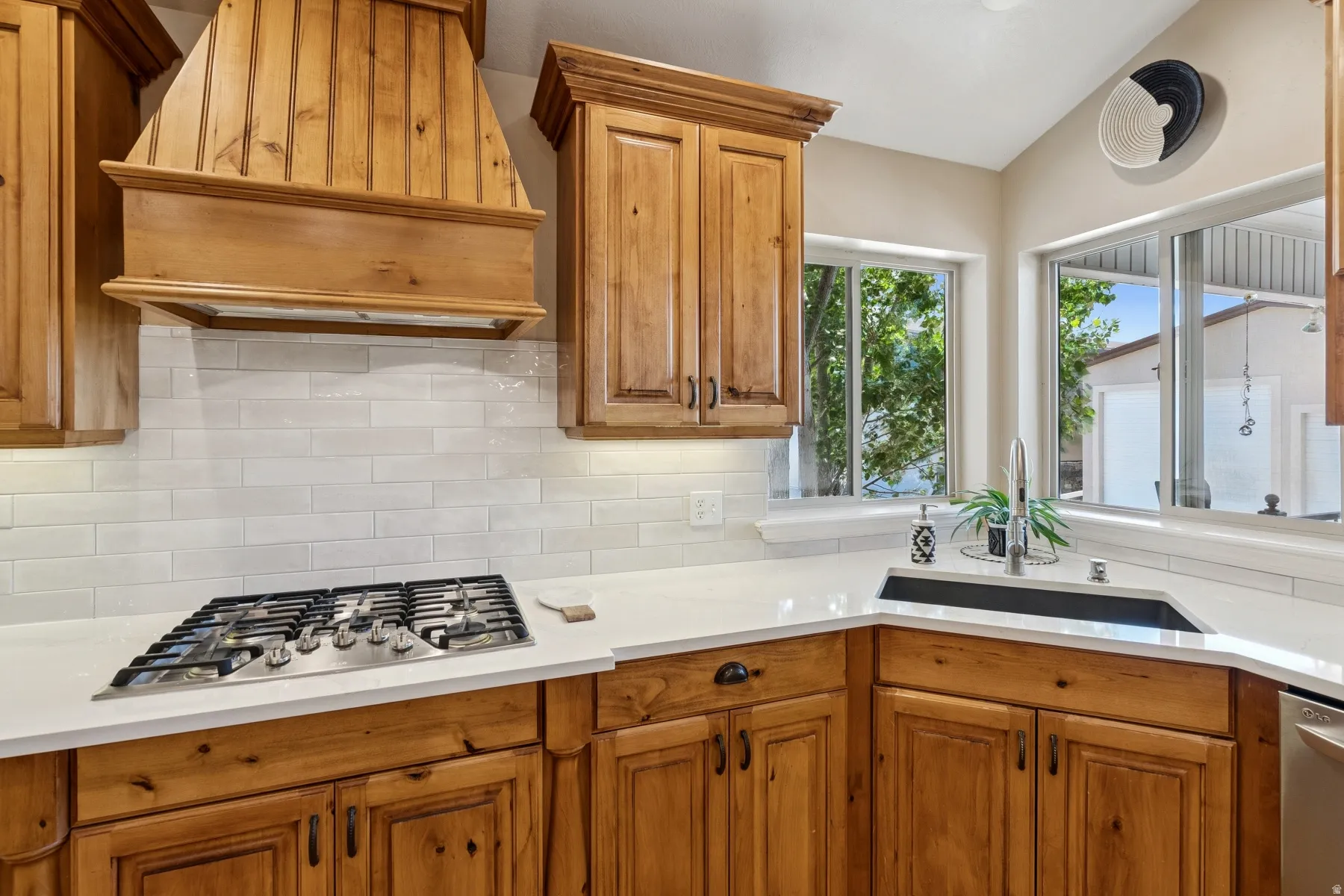 Kitchen with wood finish cabinets, stainless steel appliances, light stone counters, backsplash, and lofted ceiling