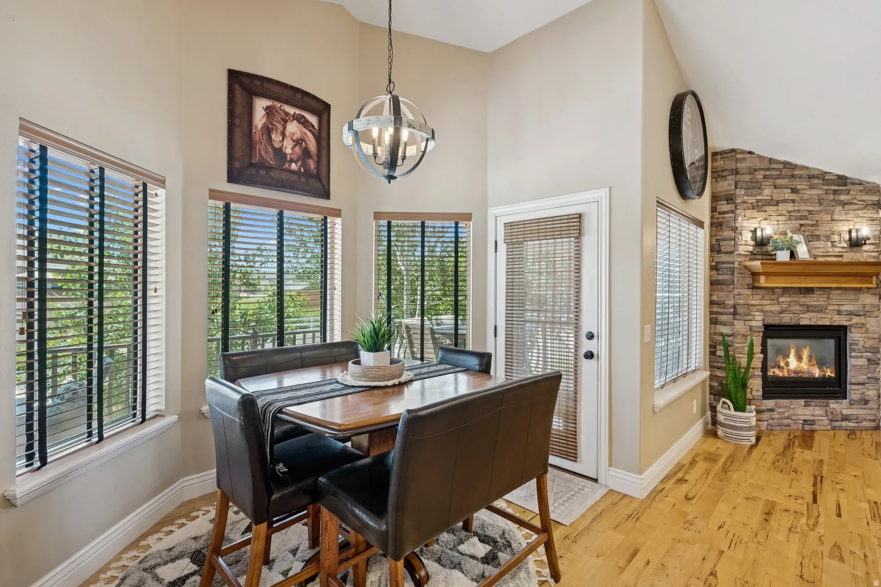 Dining room featuring vaulted ceiling, light wood-type flooring, a stone fireplace, hanging lights, and plenty of natural light