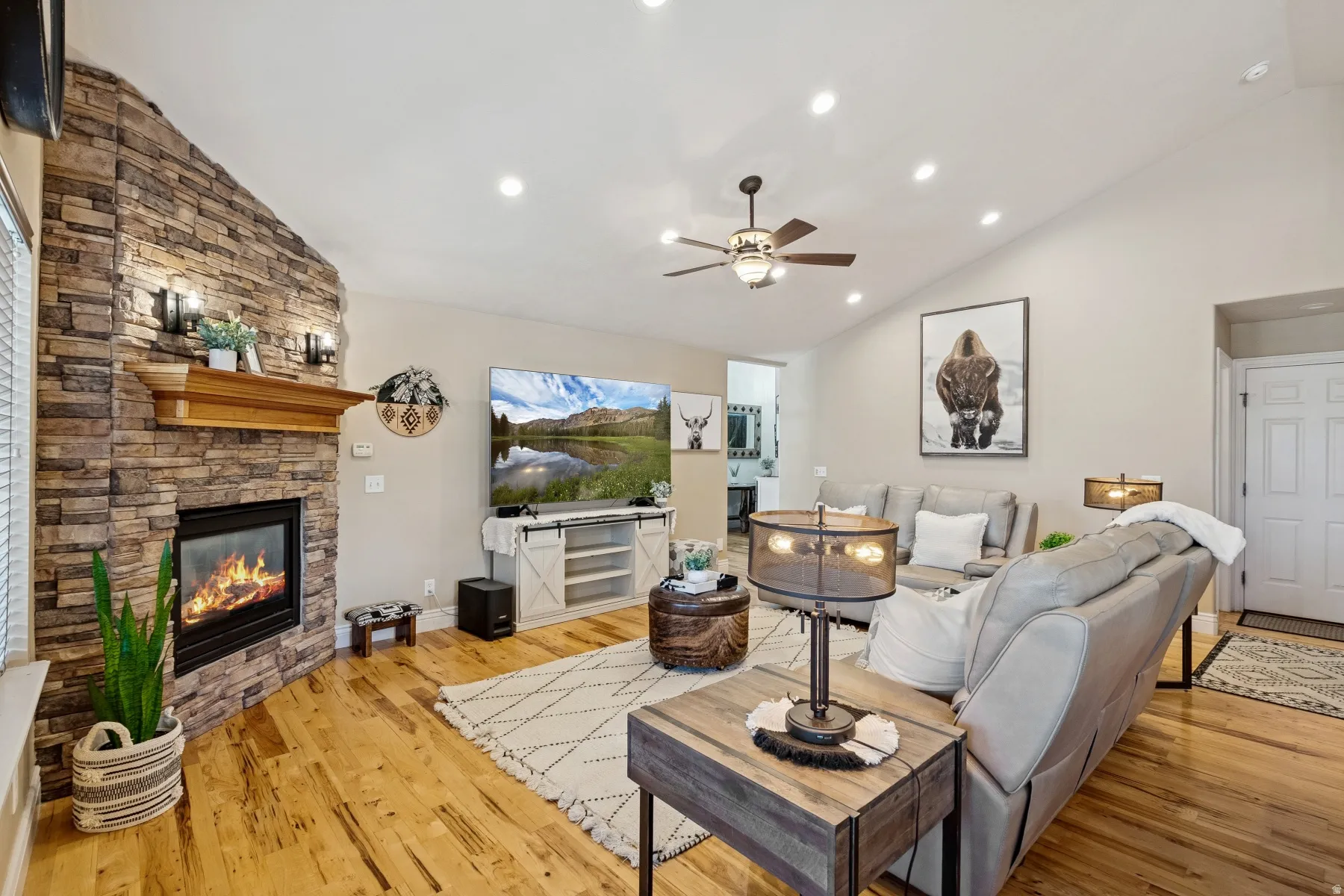 Living area featuring lofted ceiling, a ceiling fan, light wood-style floors, a stone fireplace, and recessed lighting