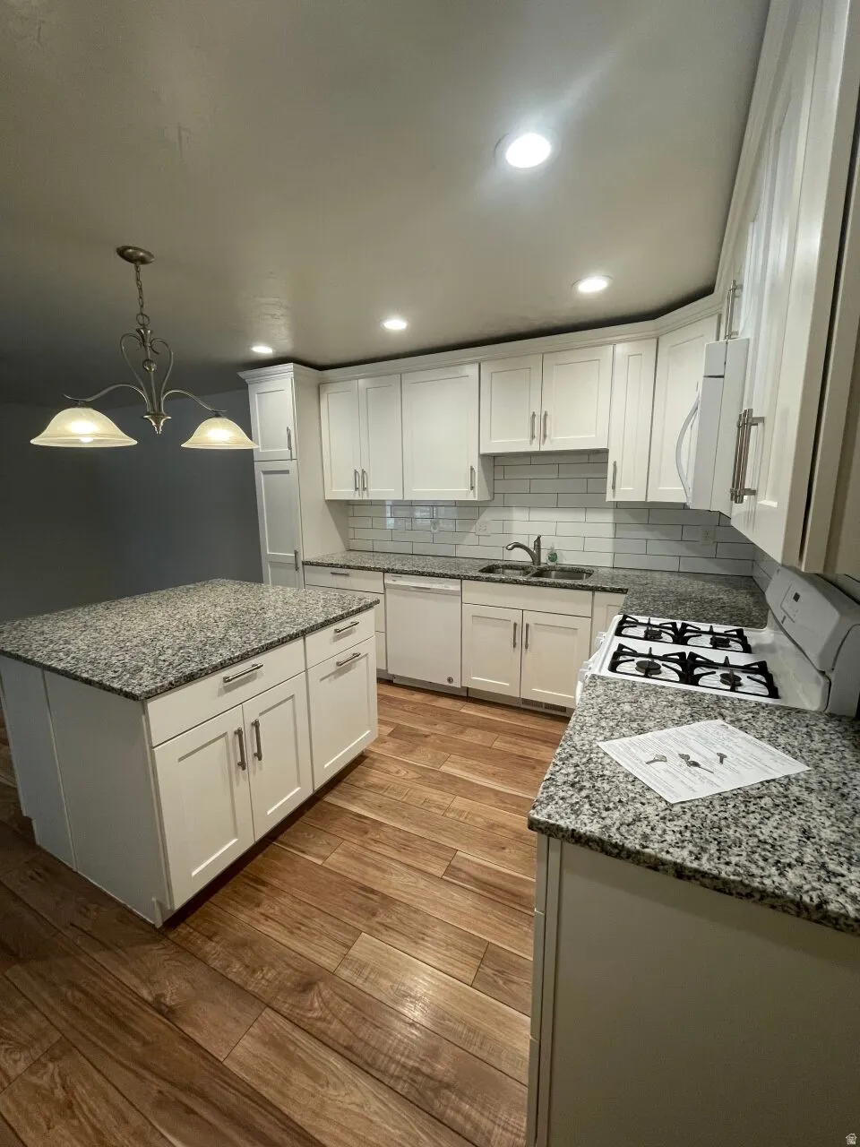Kitchen featuring dark stone countertops, a center island, white cabinetry, white appliances, and dark wood-style floors