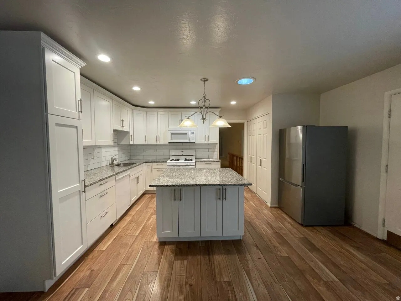 Kitchen featuring light stone countertops, white appliances, wood-type flooring, a kitchen island, and white cabinetry