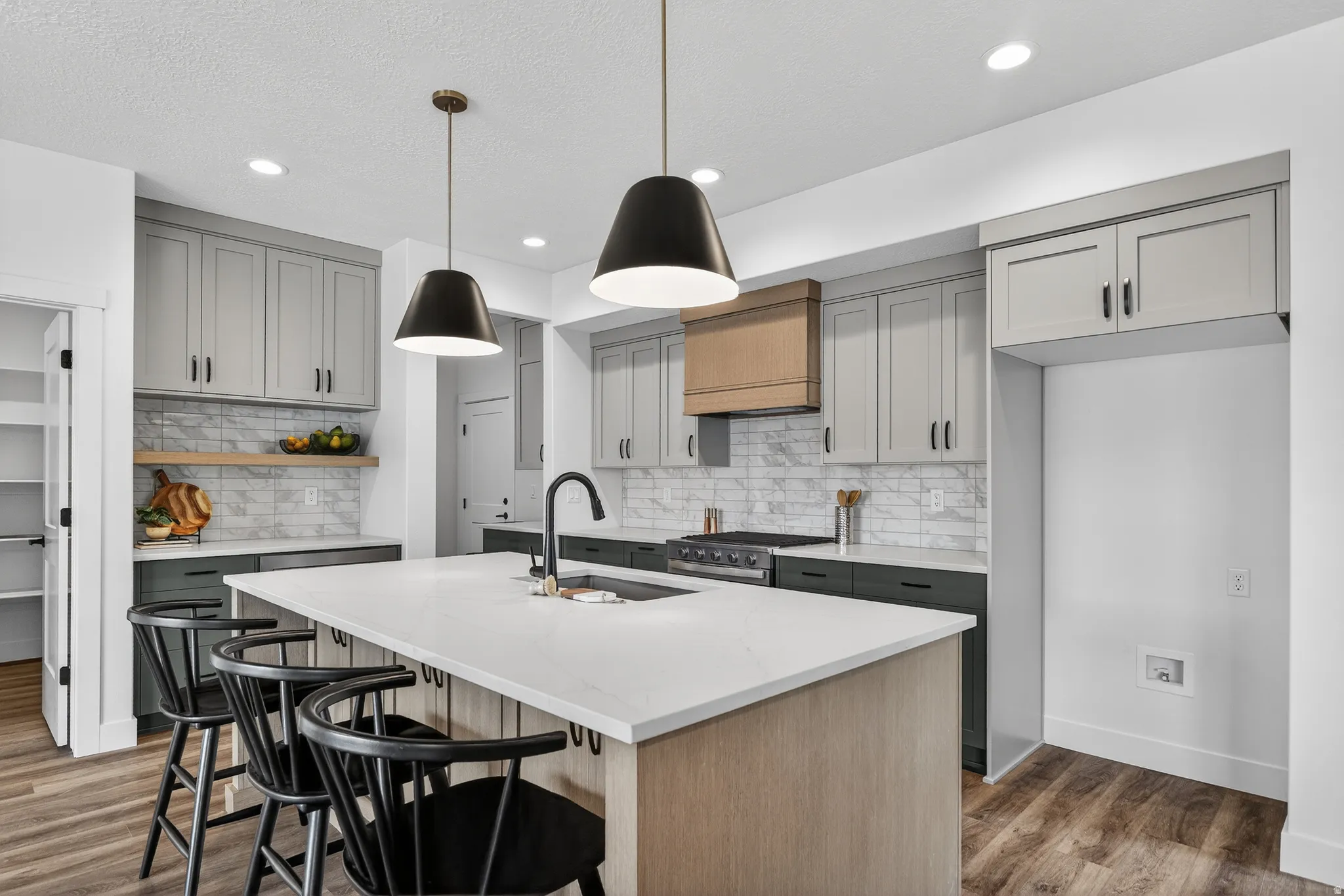 Dual tone kitchen featuring a breakfast bar area, light stone counters, dual tone cabinets, a center island with sink, and pendant lighting